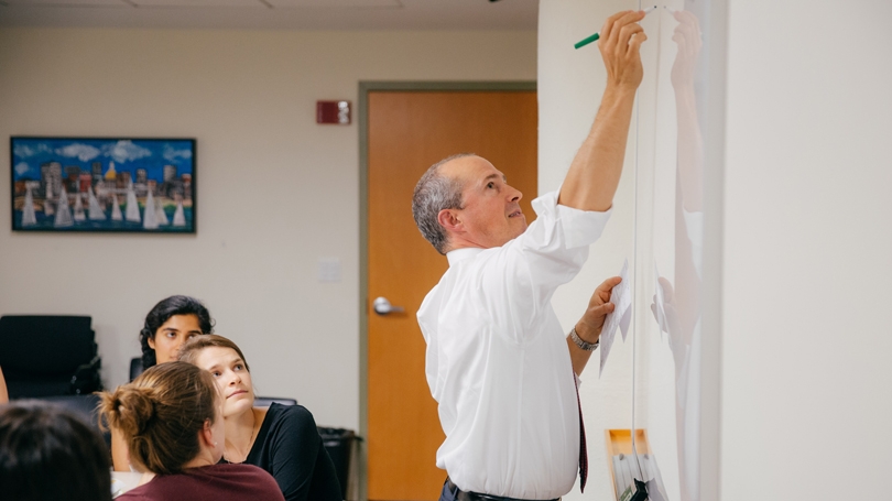Jay Gonzales ’93, writes on the blackboard during a dinner seminar for 12 public health interns.