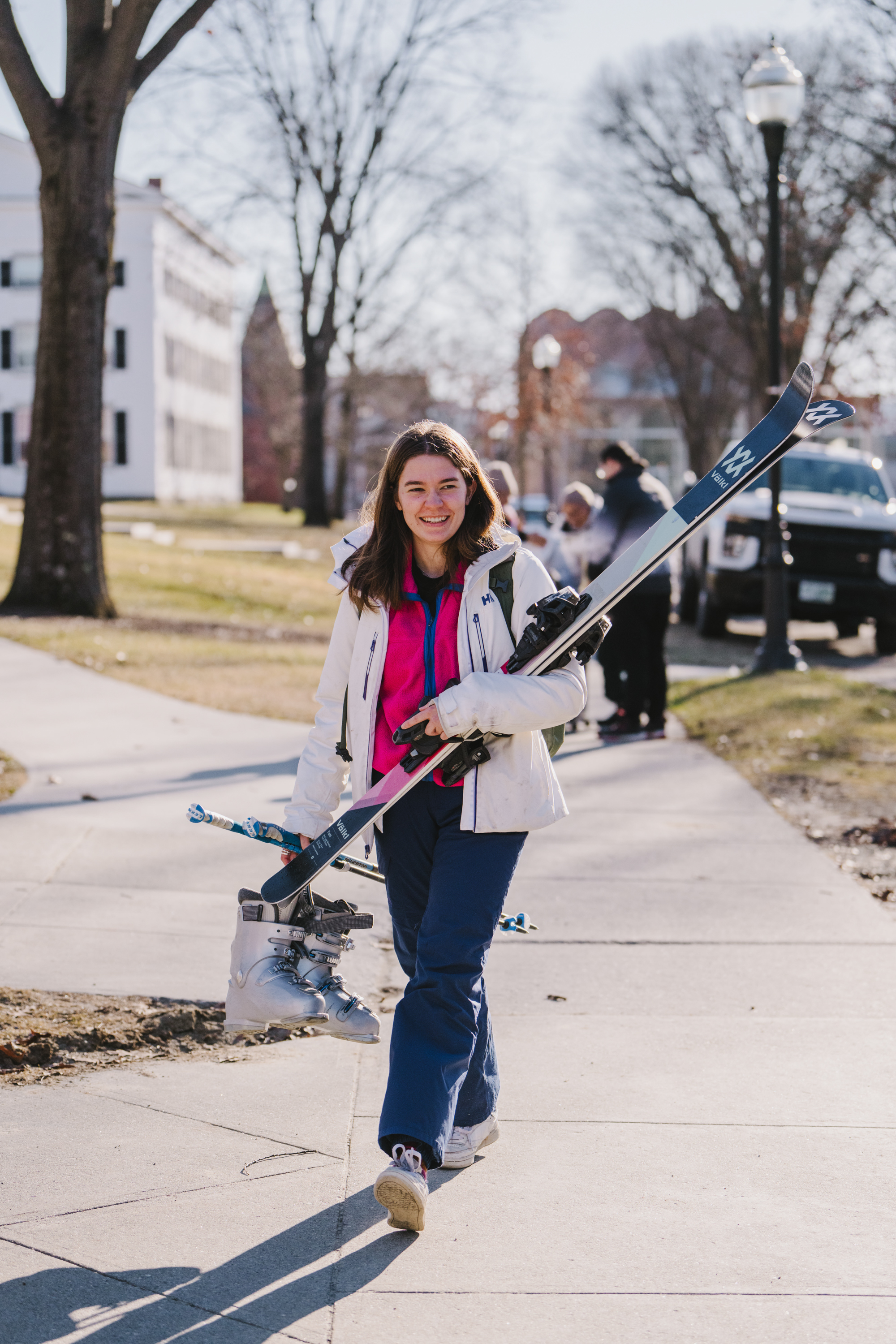 A student carries skis and boots across campus