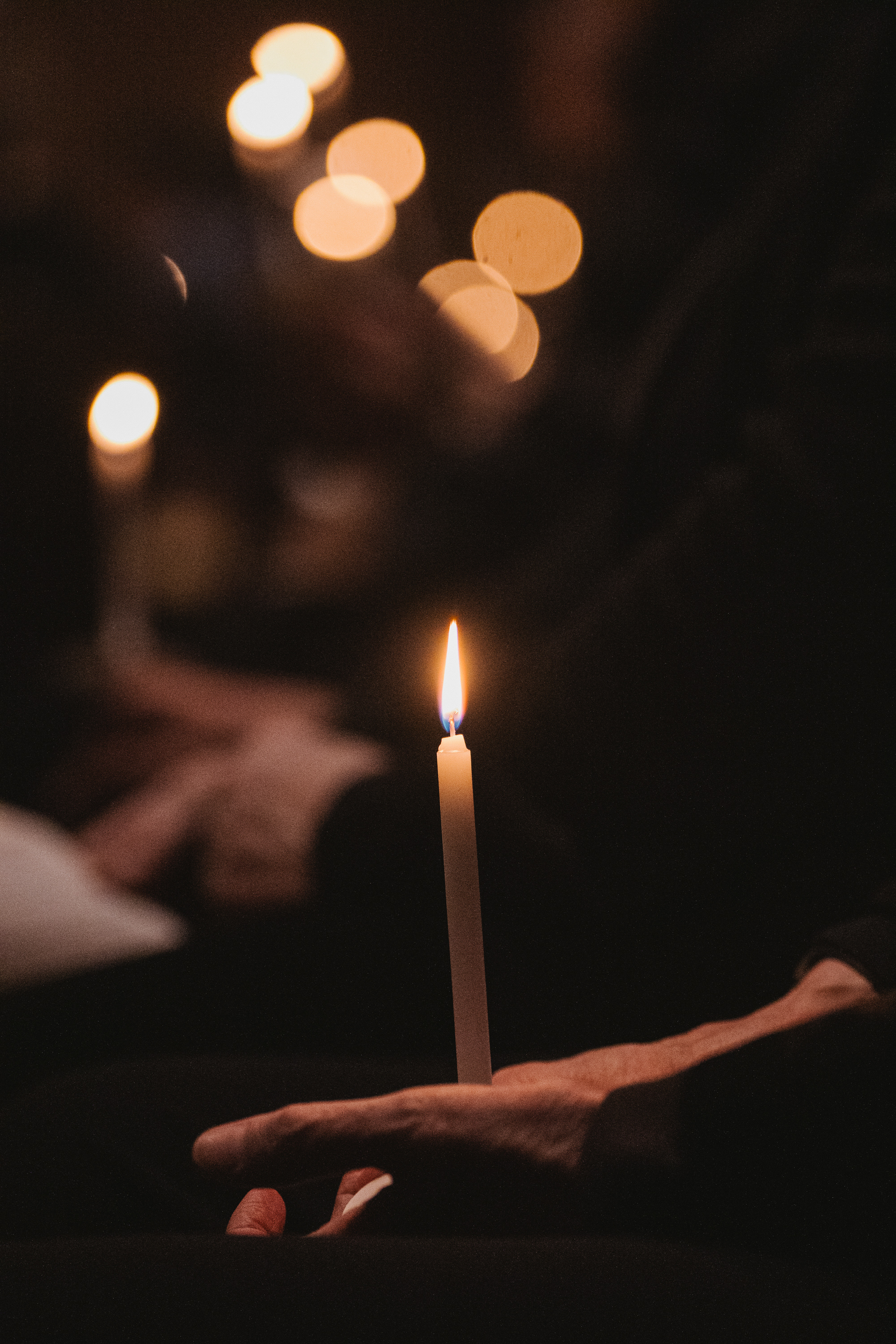 A small candle being held in front of a blurry background with other candlelight in the background