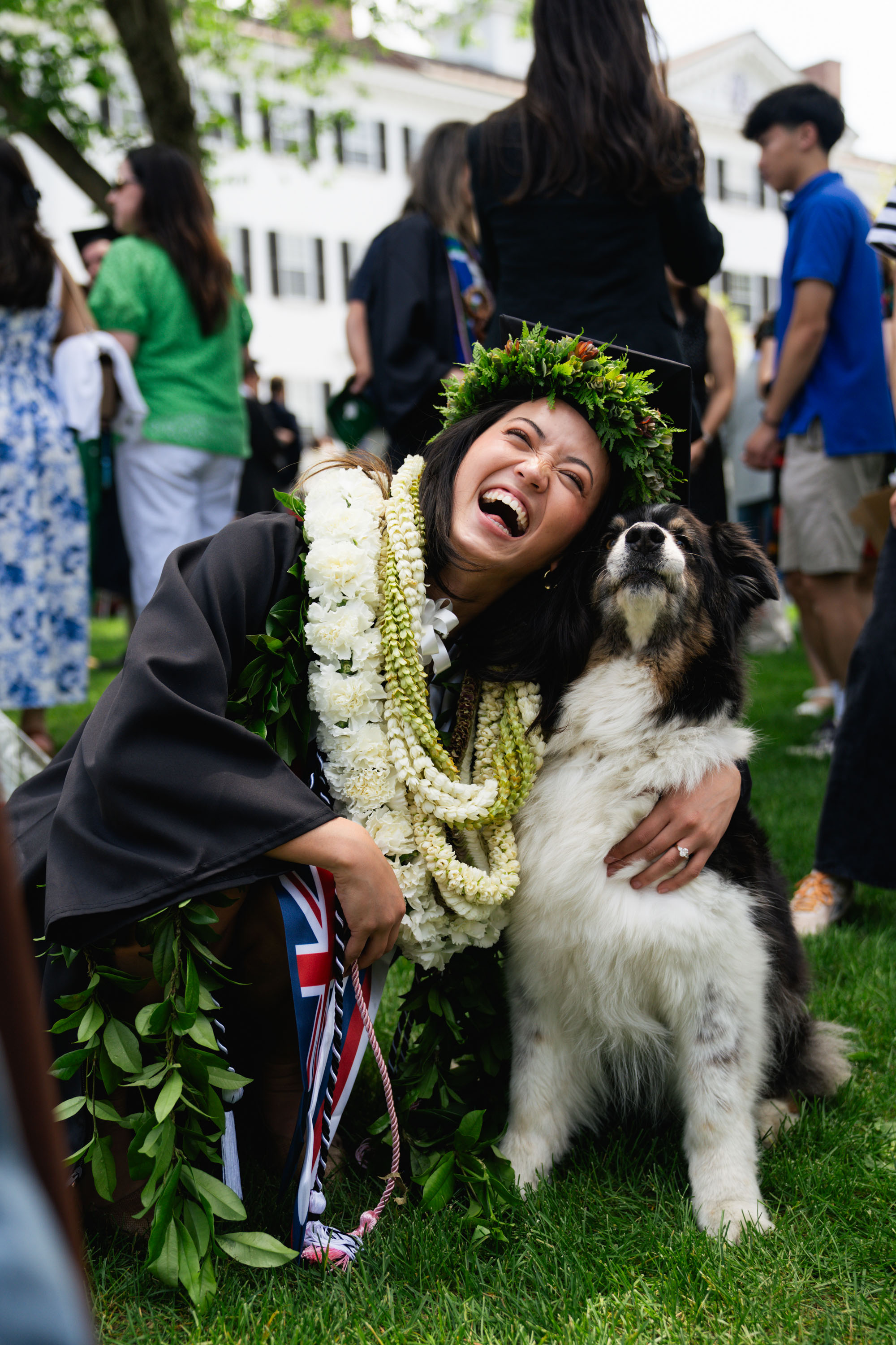 A graduate decked in leis bends down to hug a dog