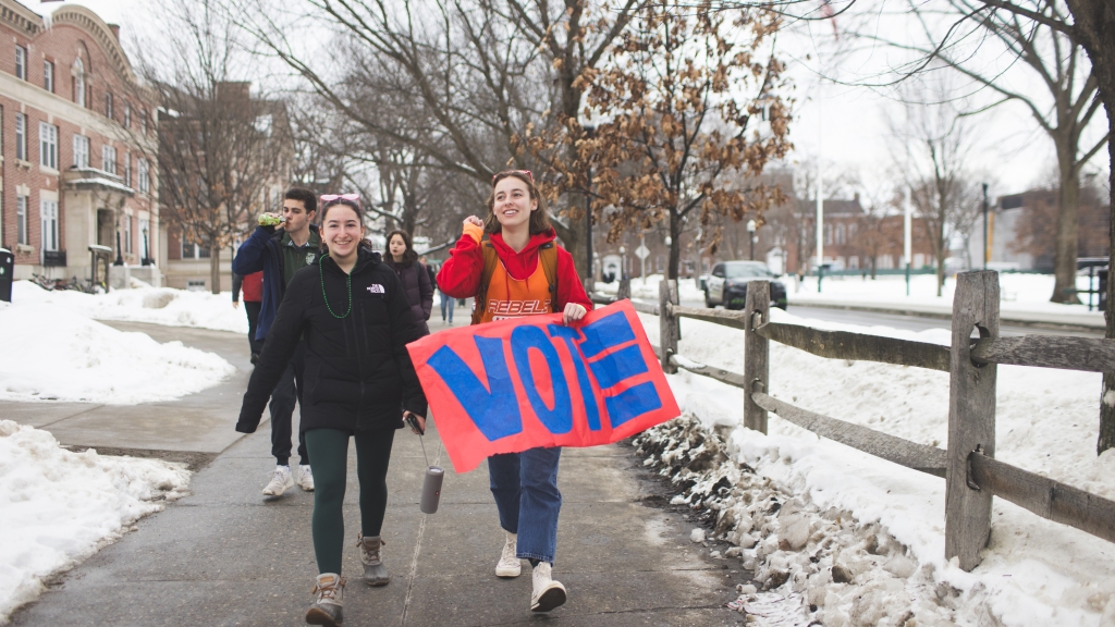Two students holding a colorful VOTE sign lead students to vote.