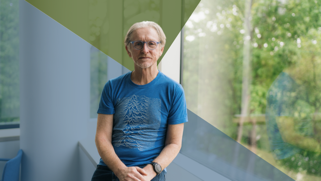 Andrew Campbell seated by a window in a blue t-shirt and glasses