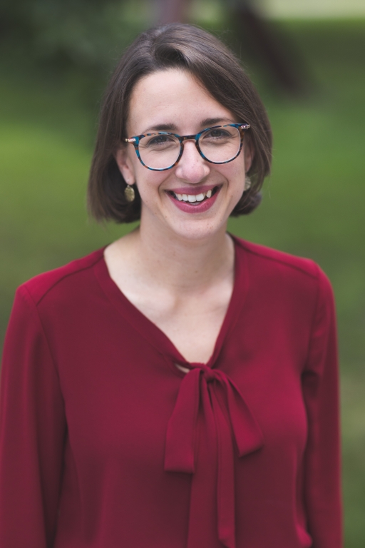 A picture of a woman smiling, wearing a red shirt and glasses. 